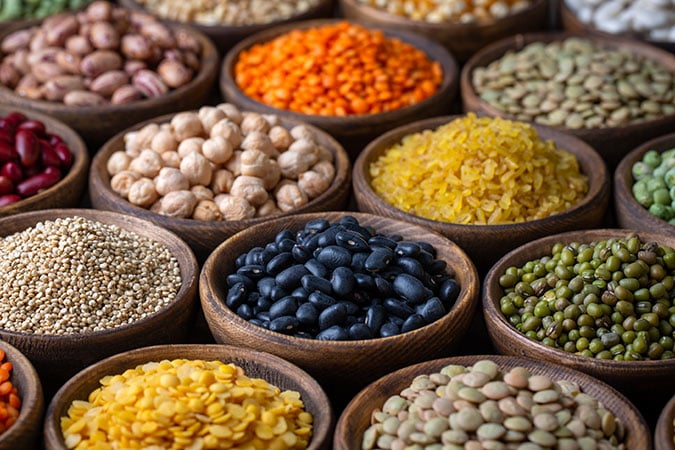 Various types of dried beans, lentils, and grains arranged in small wooden bowls, showcasing a colourful assortment of legumes and seeds.