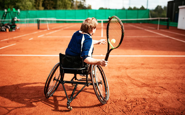 A person in a wheelchair plays clay court tennis