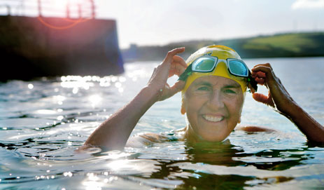 A woman smiling and swimming while wearing a swim hat and goggles