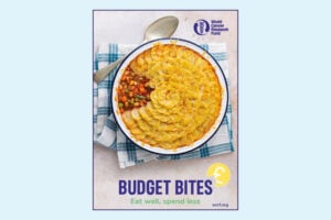 A baked dish topped with golden mashed potato sits on a blue checked cloth with a spoon. The text reads, BUDGET BITES: Eat well, spend less, and includes the World Cancer Research Fund logo.