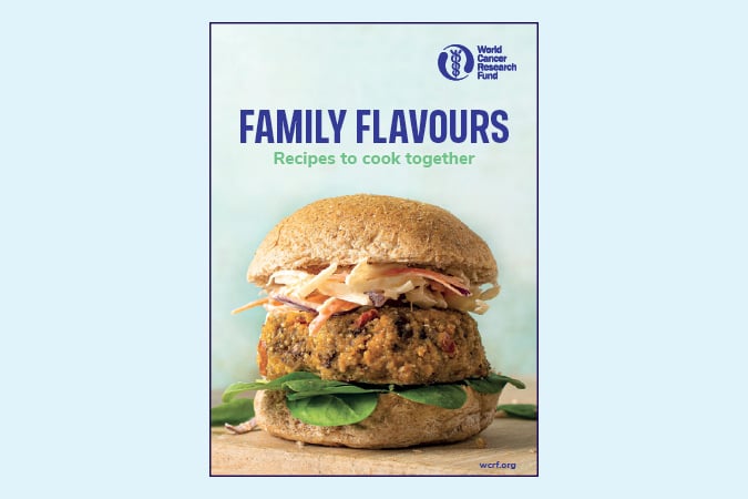 A cookbook cover titled Family Flavours: Recipes to cook together by the World Cancer Research Fund, featuring a close-up of a veggie burger with greens and slaw in a wholemeal bun.