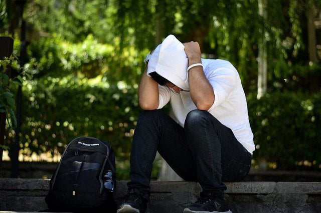 A man sits on a step hunched over with his hands and arms clutching his head