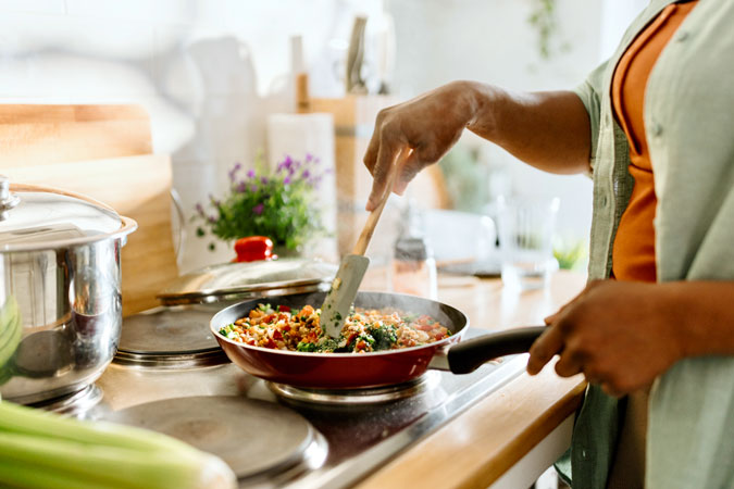 Woman cooking a colourful and nutritious quinoa stir-fry with mixed vegetables and a drizzle of olive oil.