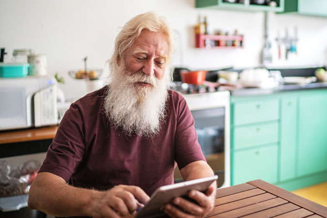 Man with white beard uses tablet at the kitchen table