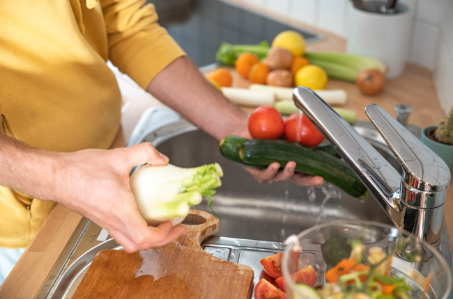 A woman washes plant foods at a sink