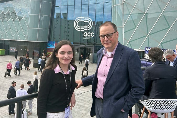 World Cancer Research Fund's Melissa Dando and Dr Scott Arthur MP stand outside the ACC Liverpool conference centre, smiling at the camera. Other attendees and the modern glass building with the ACC Liverpool logo are visible in the background.