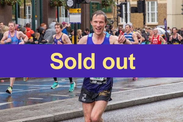 A group of runners participates in a road race on a wet street; a large purple banner with the yellow text Sold out covers the centre of the image.