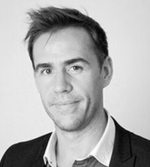 A man with short, dark hair is wearing a suit jacket and light-coloured shirt, facing the camera and smiling slightly against a plain light background, representing CUP Global.