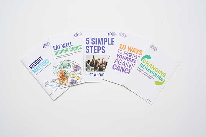 Five cancer awareness pamphlets spread out in a fan shape, each with colourful titles: “Weight Matters,” “Eat Well During Cancer,” “5 Simple Steps,” “10 Ways to Protect Yourself Against Cancer,” and “Changing Behaviours.”.