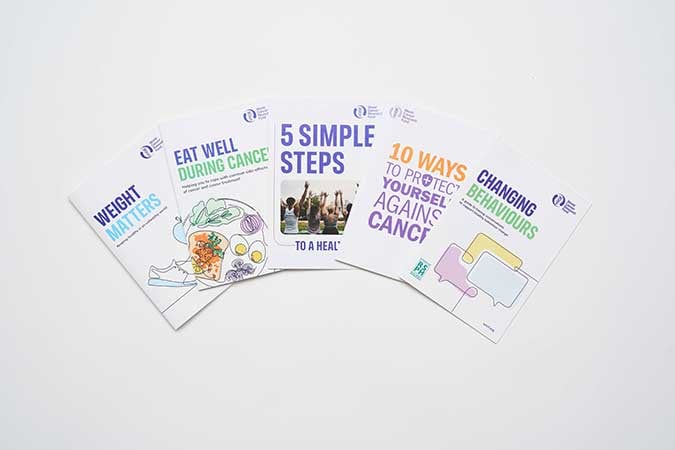 Five informational booklets about cancer prevention are spread out. Titles include: Weight Matters, Eat Well During Cancer, 5 Simple Steps to a Healthier You, 10 Ways to Protect Yourself Against Cancer and Changing Behaviours.