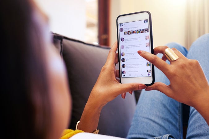 A person lounging on a sofa uses a mobile phone, scrolling through a social media feed filled with health misinformation, while wearing a large ring on the other hand. The phone screen shows various messages and photos.