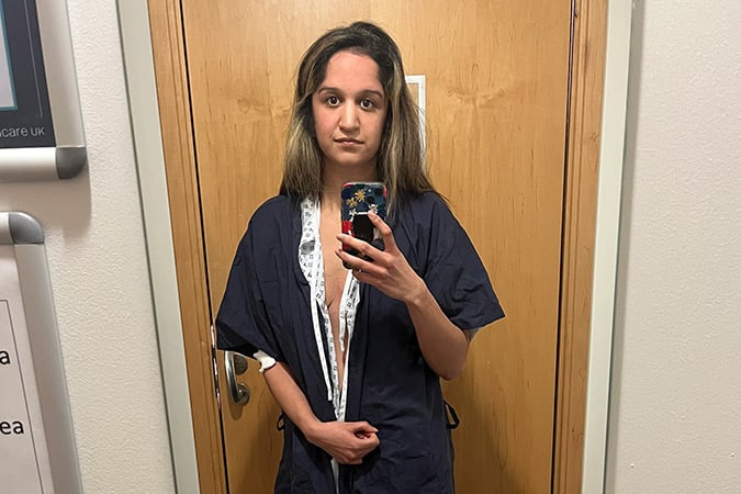 A person in a hospital gown taking a mirror selfie during a breast cancer scare.