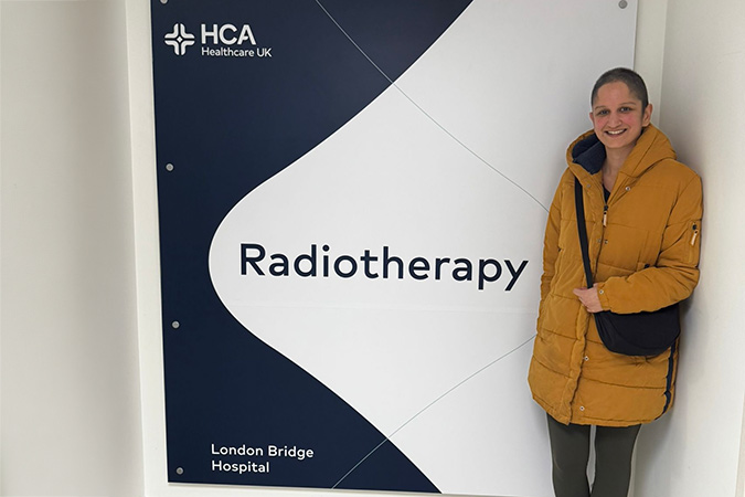 A woman wearing a yellow jacket stands next to an HCA Healthcare UK Radiotherapy sign at London Bridge Hospital, a location often visited during a breast cancer scare.