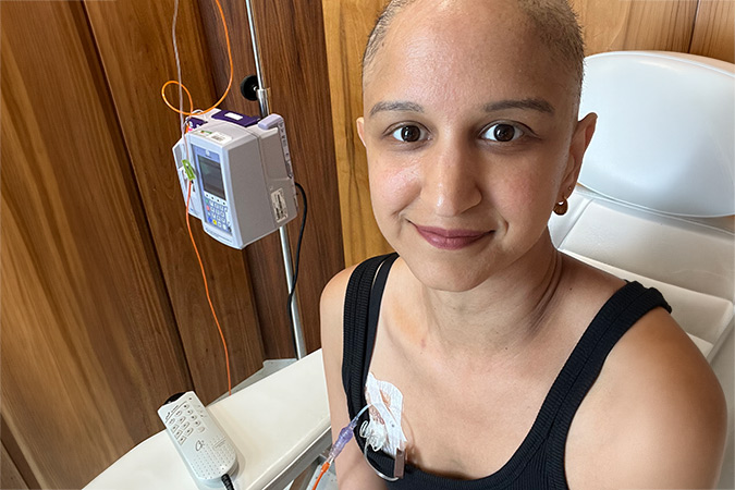 A woman with a shaved head sits in a medical chair, connected to a drip during a breast cancer scare.