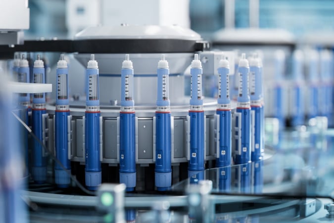 A close-up view of blue insulin pens arranged in a circular automated production machine inside a modern pharmaceutical facility highlights the precision required in manufacturing innovative treatments such as GLP-1 medicines and cancer therapies.