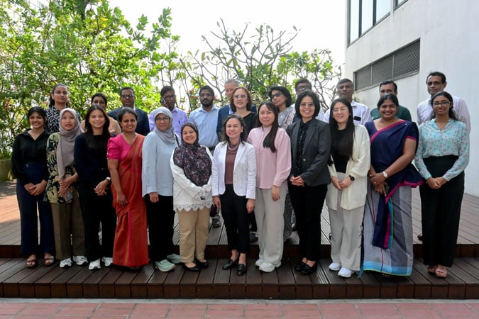 A large group of professional men and women posing for a photo on a wooden decking outdoors whilst benchmarking policies.