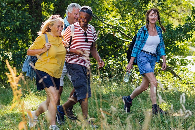 Three adults walking together on a grassy path in a wooded area.