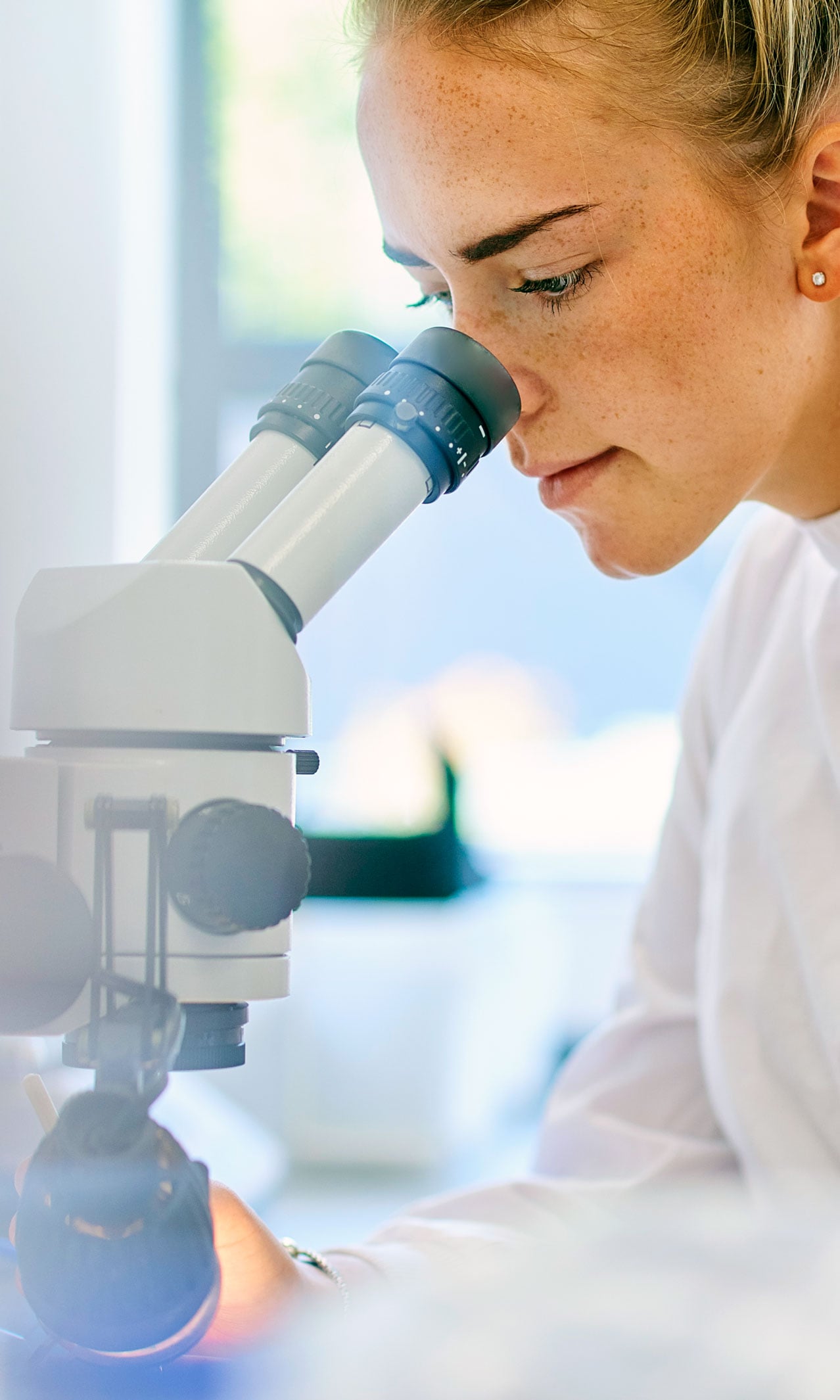 A woman in a white coat from the World Cancer Research Fund looking through the eyepieces of a microscope.