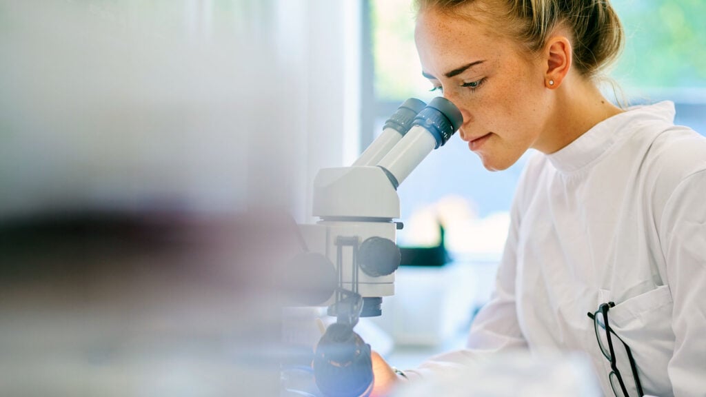 A World Cancer Research Fund researcher in a white lab coat looks through the eyepiece of a microscope.